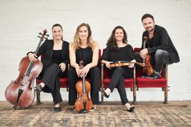 4 people in black concert dress sitting on red chairs with white brick background